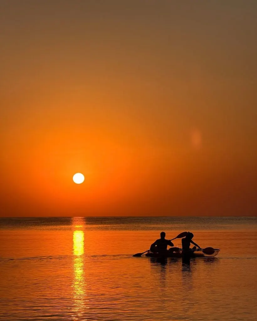 Coucher de soleil orange sur la mer, deux silhouettes au bord de l'eau