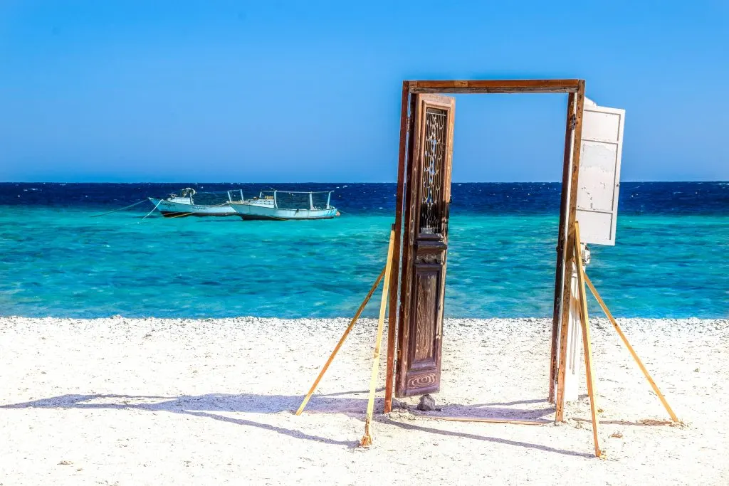 Un cadre de porte sur une plage de sable blanc, devant une eau turquoise