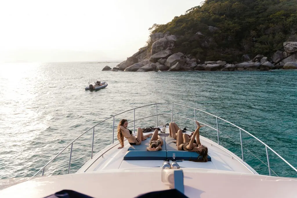 Passagers allongés à la proue d’un bateau, face à une côte boisée