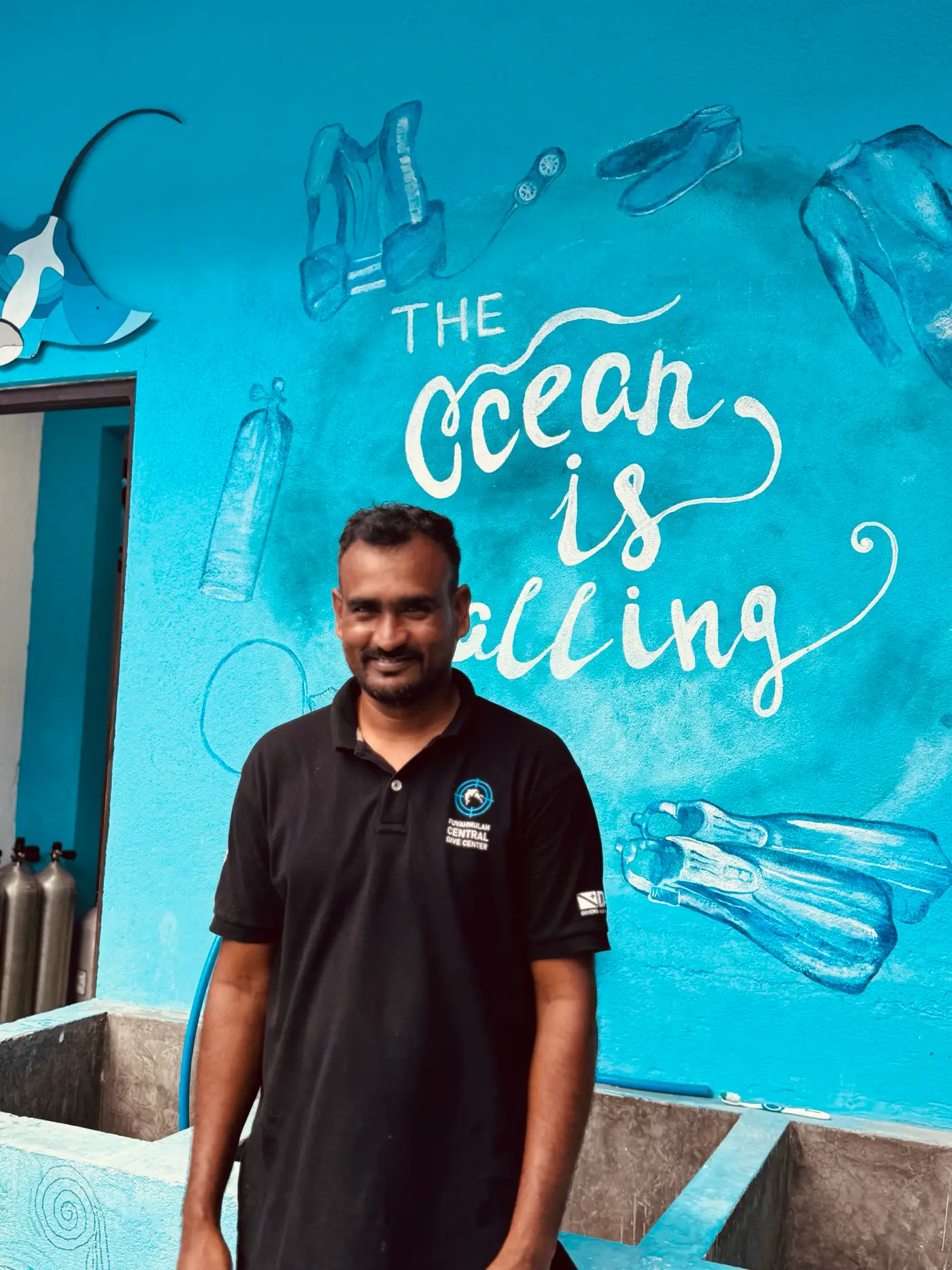 Membre de l'équipe du centre de plongée devant une fresque « The Ocean is Calling »